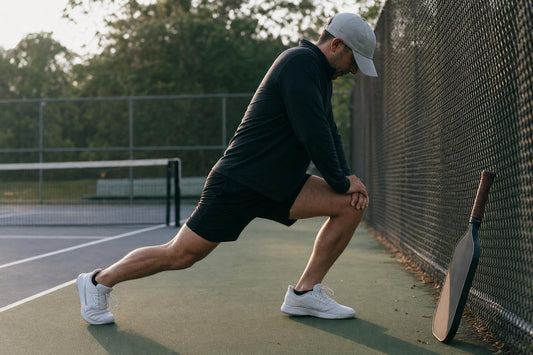 Jugador haciendo movilidad de tobillo como calentamiento junto a una pista de pickleball
