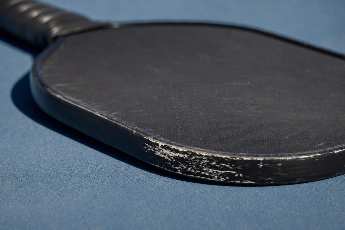 Detalle del canto y la cara de una pala de pickleball sobre una pista azul