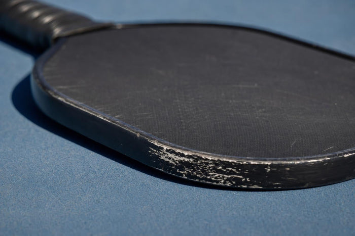 Detalle del canto y la cara de una pala de pickleball sobre una pista azul