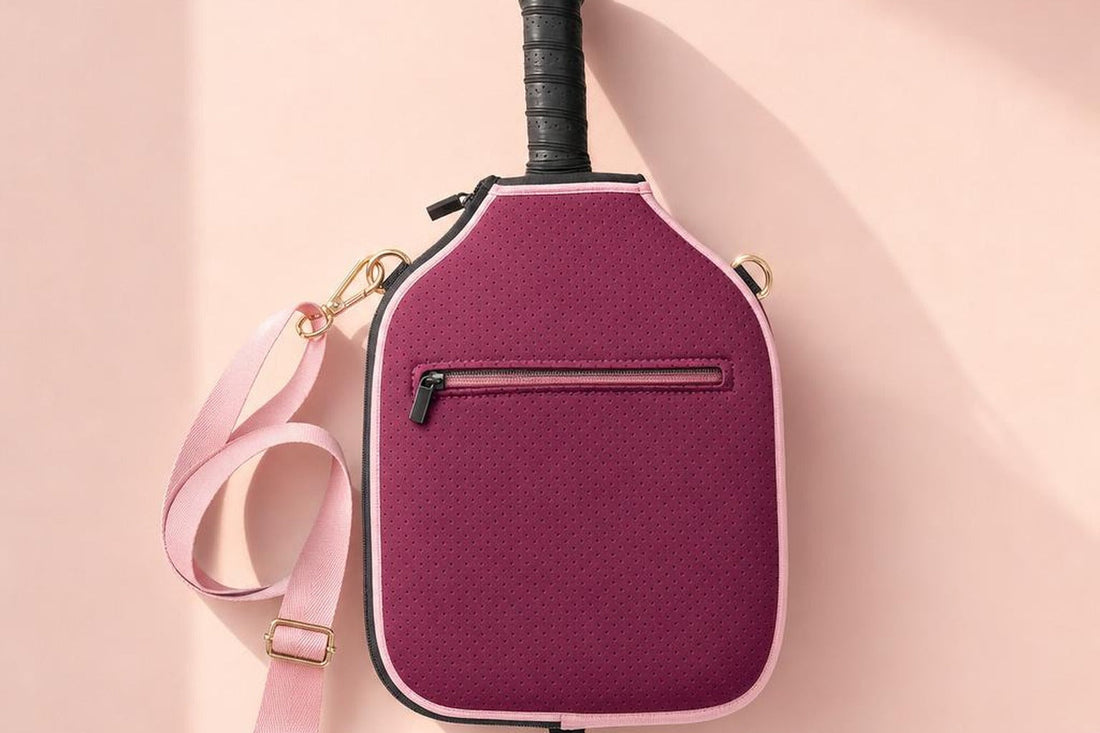 Funda de neopreno burdeos con correa rosa colgada sobre una pared rosa