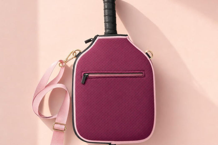 Funda de neopreno burdeos con correa rosa colgada sobre una pared rosa