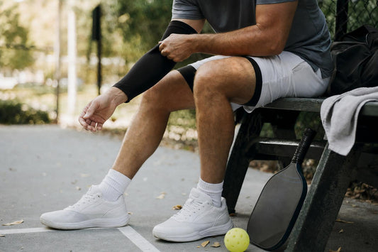 Jugador colocándose un manguito de compresión al borde de una pista de pickleball