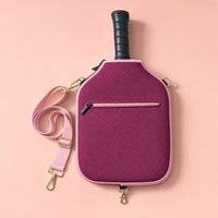 Burgundy CARRY cover with light pink strap hanging from a gold hook on a pink background