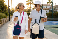 A couple of pickleball players walking to the court with coffee in hand and navy blue and cream CARRY covers worn crossbody