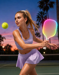 Jugadora de pickleball golpeando al atardecer con la pala ACE rosa encendida y la bola en el aire