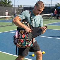 Player taking the paddle out of the floral-print RALLY backpack, slung over one shoulder on court